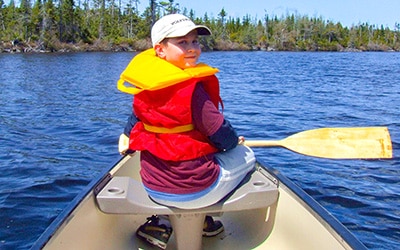young boy at Seven Peninsula Estates explores the lake via canoe
